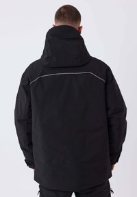 Zwarte waterdichte jas met verstelbare capuchon, gestructureerde stof en reflecterende details. Ontworpen met een losse pasvorm en een lange achterzoom.