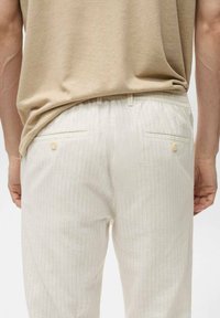 Light beige striped pants with a relaxed fit, featuring a textured fabric, elastic waistband, and two back pockets with buttons.