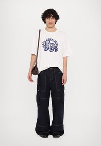 Λευκό oversized t-shirt με ναυτικές λεοπάρ γραφικές λεπτομέρειες, συνδυασμένο με σκούρο φαρδύ cargo παντελόνι που διαθέτει πολλαπλές τσέπες και αντίθετη ραφή.