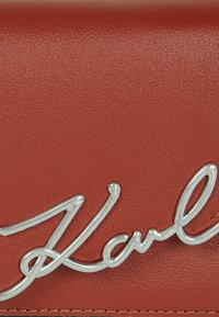 Bolso de mano de cuero rojo con un logotipo de tono plateado, textura suave y forma estructurada con acentos de diseño minimalista.