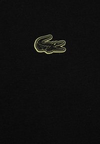 Svart tyg med ribbat mönster som har en liten, broderad krokodil-logga i grönt och svart i mitten.