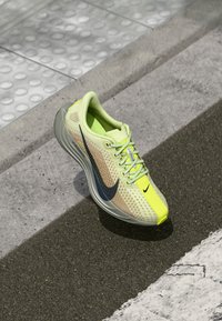 Svetložltá športová obuv s priedušným zvrškom a neonovými akcentmi, so šedou podrážkou a tmavomodrým logom Nike. Viditeľný textúrovaný povrch.