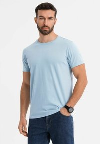 Světle modré bavlněné tričko s kulatým výstřihem a krátkými rukávy, kombinované s modrými džínami a černými hodinkami.