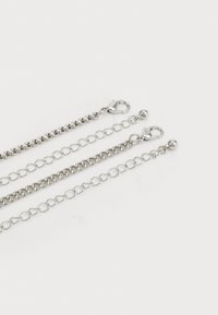 Three silver metal chains of varying designs: one with links, one with a smooth finish, and another featuring round beads, all with clasps.