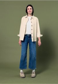 Light beige button-up shirt over a white t-shirt, paired with wide-leg blue jeans and beige shoes. Simple design, casual fit.