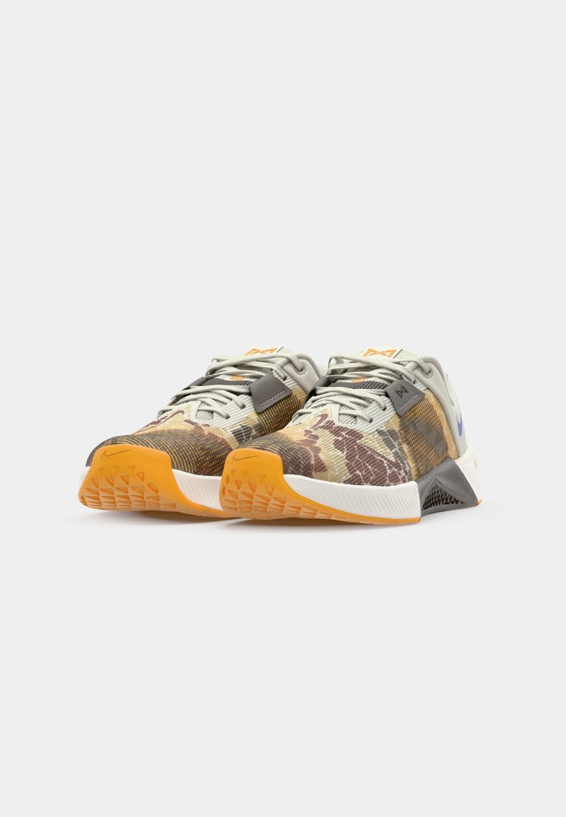 Idrottsskor med ett flerfärgat kamouflagemönster, textilöverdel, gummisula och orange detaljer. Har snören och en logotyp på hälen.