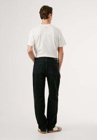 Camiseta de algodón blanca de manga corta, combinada con pantalones vaqueros negros de mezclilla con bolsillos traseros y un parche con el logo en la cintura.
