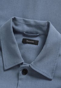 Cămașă bleu cu guler decupat, un singur nasture negru și un material texturat, cu o etichetă inscripționată "Matinique".