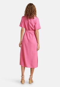 Rosa Leinenkleid mit kurzen Ärmeln, tailliertem Gürtel und seitlichen Schlitzen, das bis zur Mitte der Wade reicht. Kombiniert mit Sandalen mit Blockabsatz.
