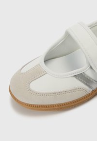 Λευκό και γκρι σουέντ π�απούτσι με στρογγυλεμένη μύτη, ελαστικό λουράκι στο πάνω μέρος του ποδιού και υφή στη σόλα από καουτσούκ. Διακριτικές ραφές καθ' όλο το μήκος.