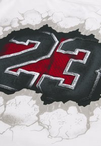 Λευκός μπλουζάκι με μεγάλο, υφασμάτινο γραφικό του αριθμού «23» σε μαύρο και κόκκινο, με ραγισμένο γκρι φόντο.