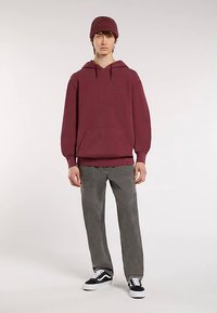 Vínová mikina s kapucí s přední kapsou, žebrovanými manžetami a logem. Kombinováno se šedými kalhotami a černo-bílými teniskami. Vínová pletená čepice.