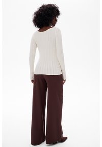 Biała prążkowana bluzka z długim rękawem zestawiona z szerokimi brązowymi spodniami. Bluzka ma okrągły dekolt i dopasowany krój.