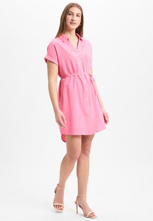 Short-sleeve, button-up pink shirt dress with a belted waist, soft texture, and a curved hem, paired with nude strappy heels.