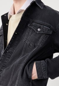 Svart denimjacka med knapplist framtill, bred krage och ficka med jacka. Har kontrasterande sömmar och en Calvin Klein-logotyp på bröstet.