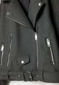 Veste de motard en laine gris foncé avec fermeture éclair asymétrique, trois poches zippées, une poche à rabat avec bouton-pression et une ceinture avec boucle en métal.