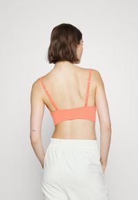 Bralette cor-de-coral com alças ajustáveis, textura kanelada e uma faixa larga. O modelo está a usar calças largas de cor clara.
