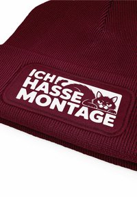 Maroon ribbed beanie with a large white embroidered patch featuring the text "ICH HASSE MONTAGE" and a stylized cat illustration.
