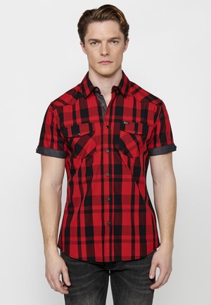 Camisa de cuadros roja y negra de manga corta con dos bolsillos en el pecho, cuello abotonado y ribete negro en contraste. Tejido de algodón, diseño ajustado.