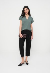 Μπλούζα μέντας με κοντά μανίκια και V-λαιμόκοψη, συνδυασμένη με μαύρο στενό παντελόνι και μαύρες μυτερές γόβες, κρατώντας μπορντό τσαντάκι.