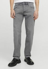 Jean en denim gris avec une coupe droite, cinq poches et une fermeture éclair. Porté avec des chaussures noires à lacets.