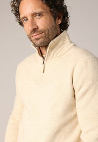Beige gebreide trui met een hoge geribbelde kraag en een rits tot halverwege, met een zachte textuur en een getailleerd ontwerp.