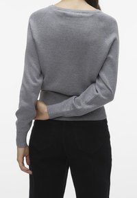 Szary dzianinowy sweter z długimi rękawami i lekko luźnym krojem. Prążkowany rant na dole i mankiety. W zestawieniu z czarnymi spodniami z wysokim stanem, z widocznym detalem z tyłu.