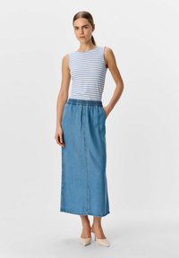 Jupe maxi en denim bleu avec une taille élastique, portée avec un haut sans manches rayé blanc et bleu et des escarpins beiges à bout pointu.