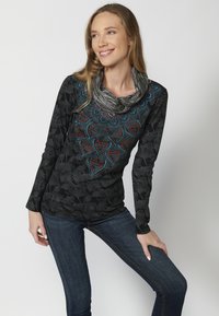 Schwarzer Langarmoberteil mit strukturierter Blumenmuster, verziertem Ausschnitt mit blauen und roten Details, kombiniert mit dunklen Jeans.