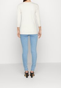 Weiß gestreiftes Langarmoberteil, hellblaue enge Jeans und schwarze Absatzsandalen. Keine sichtbaren Muster oder Akzente auf der Kleidung.