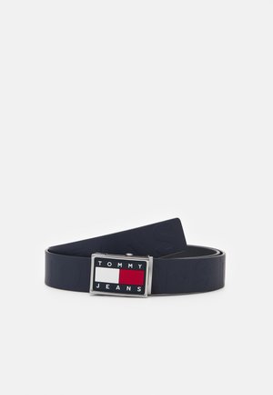 Ciemnoniebieski pasek zwinięty, z prostokątną srebrną klamrą, na której znajduje się czerwona, biała i granatowa logo oraz napis Tommy Jeans.