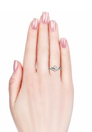 Silberring mit einem zentralen Diamanten und einem Chevron-Design, flankiert von kleineren Steinen. Hand mit pink lackierten Nägeln, die den Ring zeigt.