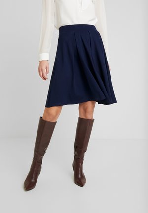 Gonna plissettata navy con vita alta, realizzata in un tessuto fluido, abbinata a stivali in pelle marrone al ginocchio.