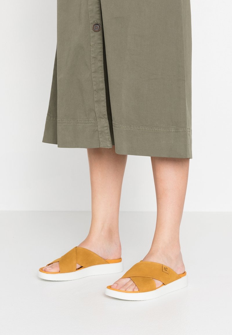 Sandales à glissière en suède beige avec un design croisé ; semelle blanche avec un léger rehaussement ; surface texturée ; bout ouvert.