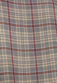 Le tissu écossais présente des carreaux gris, jaunes et rouges, avec un tissage texturé et des lignes horizontales et verticales bien définies formant un motif.