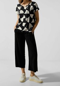 Top noir et blanc à manches courtes avec un motif géométrique, associé à un pantalon large noir et des baskets légères. Coupe décontractée et détail à cordon de serrage.