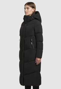 Langer schwarzer Puffer-Mantel mit Kapuze, der horizontale gesteppten Abschnitte, seitliche Reißverschlusstaschen und eine schlanke Silhouette aufweist.