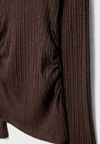 Temno rjav rebrast pleten material z nabranim detajlom ob šivu, ki prikazuje teksturo in raztegljivost v posnetku od blizu.