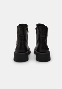 Botas de cuero negro hasta el tobillo con un acabado suave, que presentan una punta redondeada y una suela de goma texturizada, realzadas con cremalleras laterales.