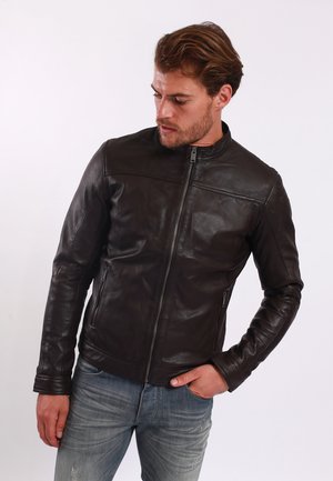 Brown leather jacket with a fitted design, high collar, front zipper, and subtle stitching details. Worn over light-wash jeans.