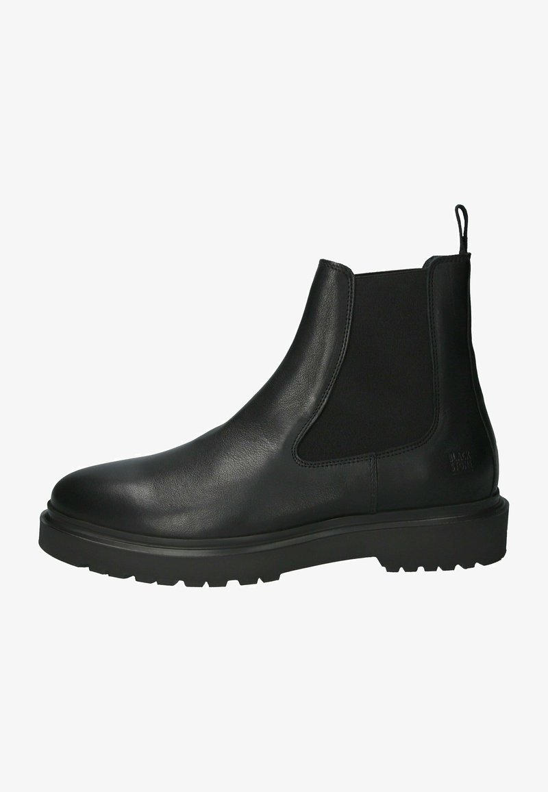 Botín Chelsea de piel negra con paneles elásticos a los lados, punta redonda y suela de goma texturada. Presenta un lazo en el talón para facilitar su calzado.