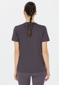 Lyhythihaiset, pyöreäkauluksiset t-paidat tumman violetista pehmeästä kankaasta; takanäkymä näyttää letitetyn hiustyylin ja saumatonta olkapään muotoilua.