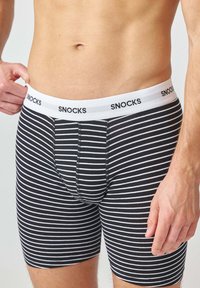 Boxer briefs a righe bianche e nere con una banda elastica bianca che presenta il marchio "SNOCKS" in lettere nere. Tessuto morbido.