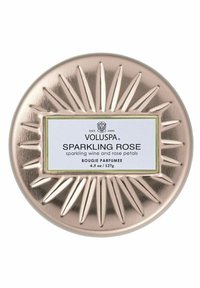 Pyöreä, metallinen kynttiläkippo, jossa on ruusukultainen viimeistely ja auringonsäteitä muistuttava koriste. Etiketissä lukee "Voluspa Sparkling Rose" mustalla ja valkoisella.