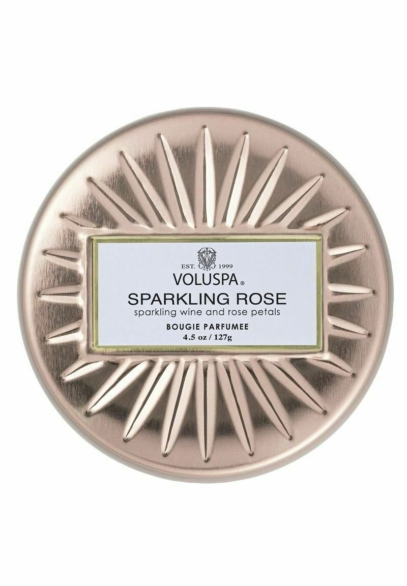 Pyöreä, metallinen kynttiläkippo, jossa on ruusukultainen viimeistely ja auringonsäteitä muistuttava koriste. Etiketissä lukee "Voluspa Sparkling Rose" mustalla ja valkoisella.