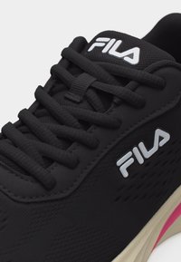 Κοντινό πλάνο μαύρου αθλητικού παπουτσιού FILA με κορδόνια, εμφανή λογότυπα FILA στη γλώσσα και στην πλευρά, και τμήμα μπεζ σόλας με ροζ λεπτομέρεια.
