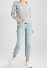 Grå sweatshirt med texten "inte mitt problem", i kombination med ljusblå, cropped jeans och vita sneakers. Mjuk tygkvalitet, avslappnad passform, minimal detaljering.