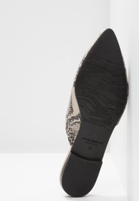 Chaussure plate à bout pointu avec dessus en imprimé serpent et semelle en caoutchouc noire marquée "Vagabond Shoemakers" taille 37, posée contre un mur d'angle blanc.