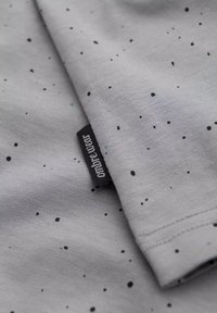 Šedá látková košile s malými černými a modrými skvrnami. Obsahuje černou štítku s označením "ombre wear" na přehnutém rohu. Hladká textura.