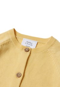 Gelbe Strickjacke aus weichem Material mit Rundhalsausschnitt, gerippten Kanten und zwei Holzknöpfen auf der Vorderseite. Etikett sichtbar.